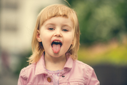 Beautiful 2 year old girl showing tongue in the street close up
