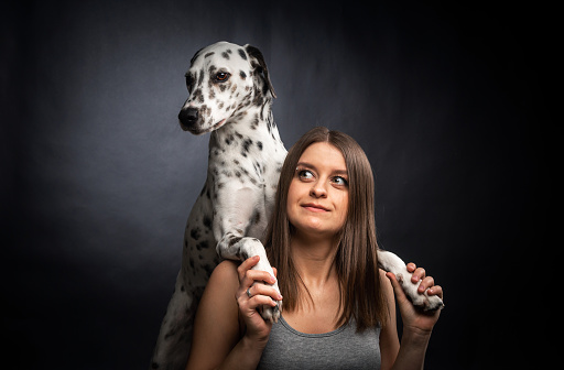A young pretty woman is playing with her Dalmatian pet, isolated on a black background. Studio portrait of the dog and the owner.