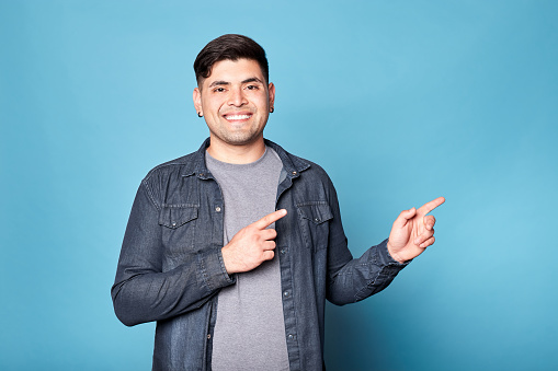 Portrait of a happy latino young man smiling and showing copy blank space isolated over blue background. Copy space.