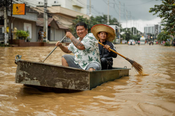 Men in a boat holding brooms used as paddles in a flooded street in Chiang Mai, Thailand.