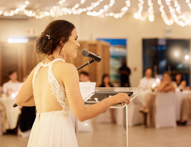 istock Wedding speech and happy bride with microphone speaking to marriage party reception guests. Cheerful and caring married woman love story presentation at banquet with friends and family. 1432006172