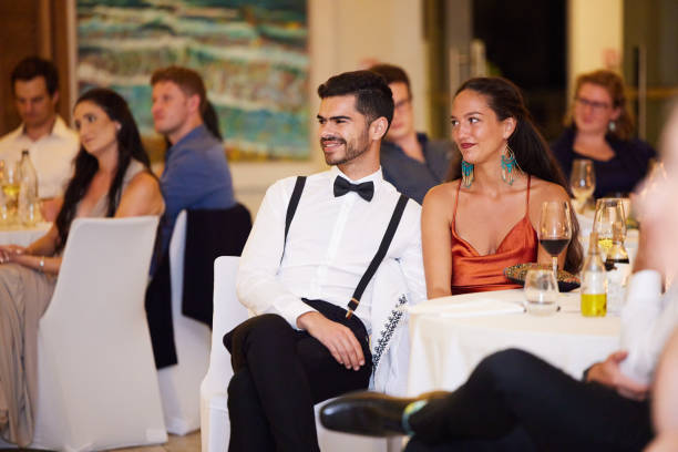 Wedding, couple and celebration with guests, audience or a crowd at a marriage ceremony, reception or celebration event. Love, romance and tradition with a man and woman sitting in an indoor venue