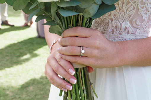 Wedding, bouquet and ring of a bride at her ceremony in nature in a garden standing at the altar. Closeup of woman hands with a manicure and jewelry holding flowers at her marriage celebration event.