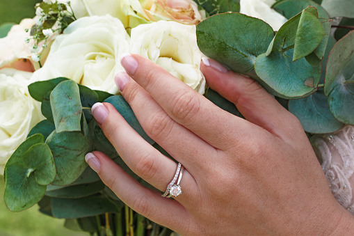 Wedding, flowers and bride with ring on hand, floral beauty closeup and cropped. Gold, diamond and a white rose flower bouquet in hands, celebration of love and marriage, a woman on a special day.