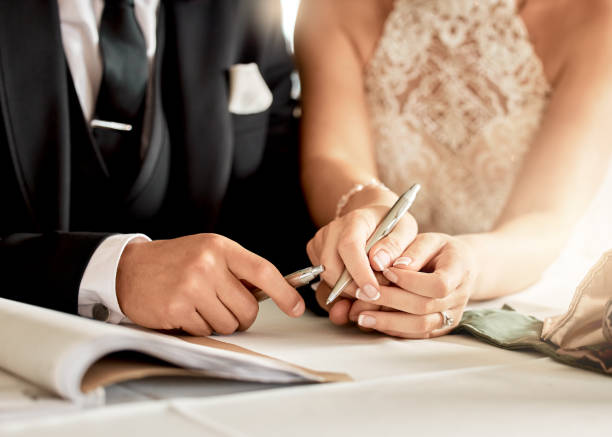 couple sign wedding certificate, marriage registration and document paper for legal union. closeup bride, groom and hands writing contract for celebration of love, commitment and agreement together - wedding stockfoto's en -beelden