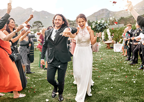 Couple holding hands, wedding celebration and nature event in summer with family, happy at marriage reception in mountains and smile for love. Man and bride walking in aisle with friends to celebrate