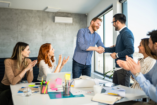 Young modern men in smart casual wear shaking hands and smiling while working in the creative office.