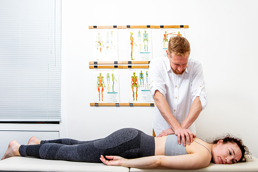 Male osteopath (chiropractor) treating back problem of a young woman lying down on a massage bed. Can illustrate the concept of Osteopathy, Alternative medicine, Physiotherapy, pain relief.