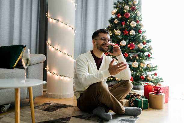 istock Young man sitting by Christmas tree and using his smart phone 1432013201
