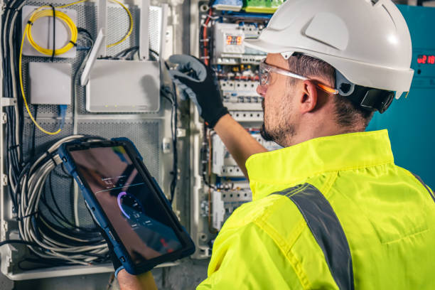 istock Man, an electrical technician working in a switchboard with fuses, uses a tablet. 1432014329