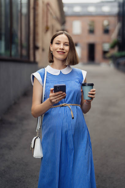 istock Modern pregnant woman walking among office buildings using a smartphone 1432019062