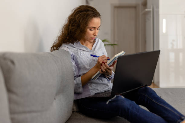 istock Woman sitting on a sofa and writing something in the note pad 1432019284