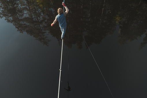 The tightrope walker walks over the water. Aerial view. Themes of slackline, highline and waterline. Extreme activity.