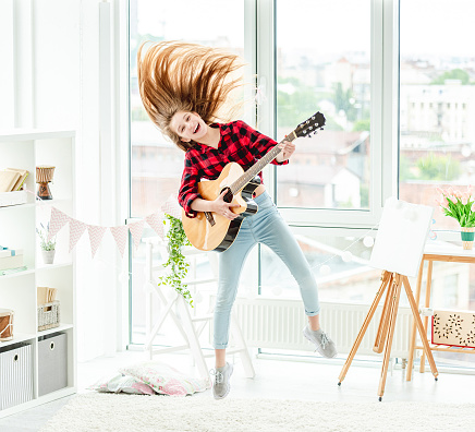 Teenage girl with guitar in high jump at home