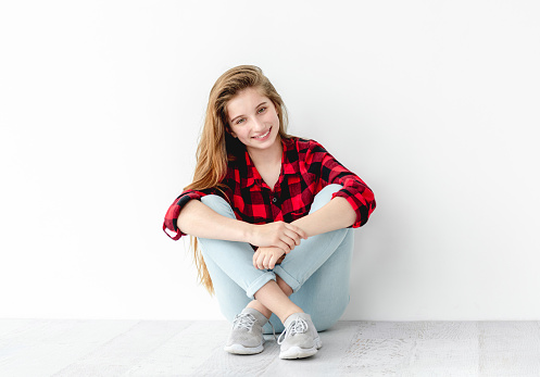 Smiling teenage girl sitting on floor on white wall background