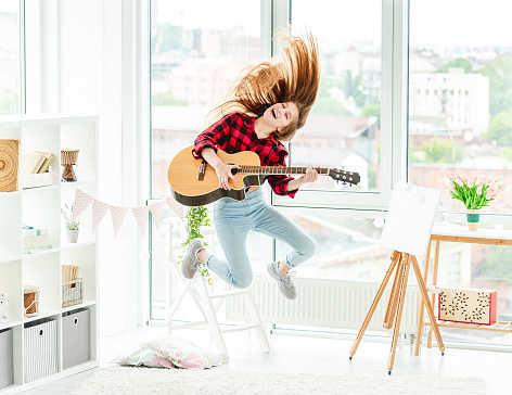 Cute young girl with guitar in high jump at home