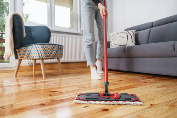 woman cleaning wooden floor with mop in living room stock photo