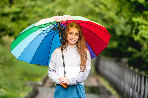 Portrait of young girl under colorful umbrella in rainy park