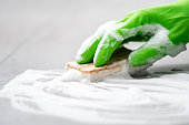 gloved hand cleaning floor with sponge and detergent foam, closeup