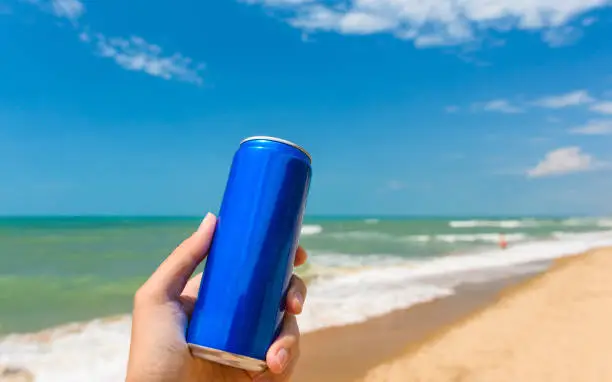 Photo of A jar with a cold drink in hand against the backdrop of the sea shore. Close-up.