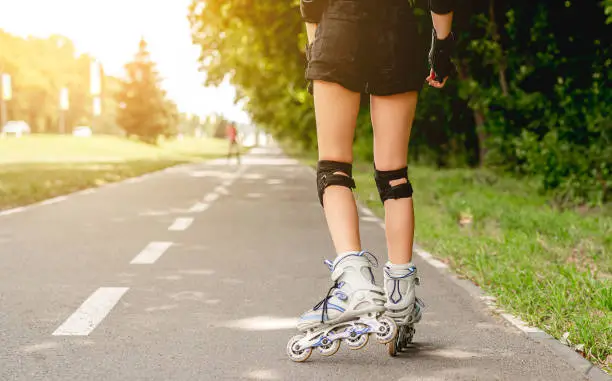 Girls legs in line roller skates in park at sunset, partial view