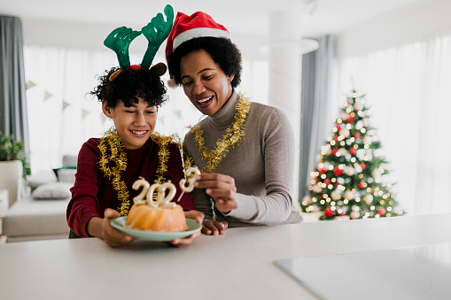 Mother and son celebrating Ney Year  and eating Christmas cake with golden candles shaped 2023 numerals