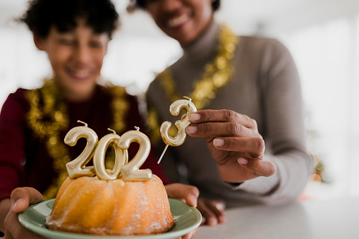 Close up of Mother and son celebrating Ney Year  and eating Christmas cake with golden candles shaped 2023 numerals