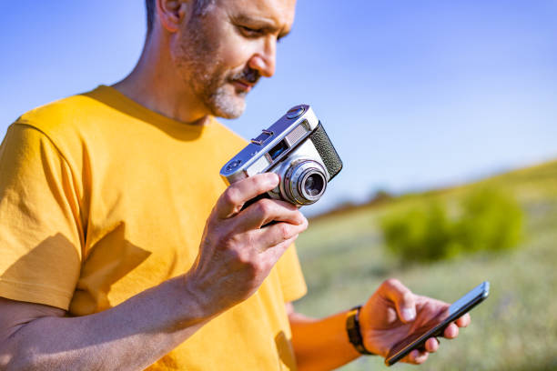 Madrid Spain. May 23, 2022. The current and the old. Man using his mobile phone while holding an analog negative film camera with the other hand. Country and sunny setting