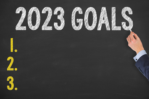 Human Hand Writing New Year 2023 Goals on Chalkboard Background
