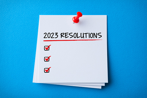 White Sticky Note With New Year 2023 Resolutions And Red Push Pin On Blue Cardboard Background