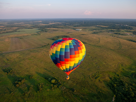 A colorful air balloon is flying in free flight over the field. Bird's-eye view. Multi colored balloon in the blue sky.