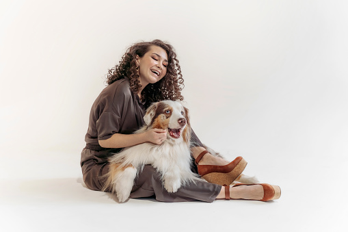 Young smiling woman playing with her dog , she is cuddling her pet. Australian Shepherd Dog and young Curly woman,