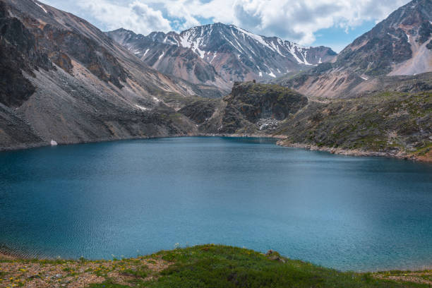 istock Deep mountain lake of phantom blue color among sharp rocks and high mountains in changeable weather. Wonderful dramatic view from sunlit grassy hill to deep blue alpine lake and rocks under cloudy sky 1432057853