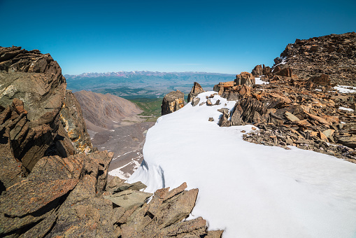 Vertigo view from precipice edge with snow cornice and steep couloir to large mountain range under blue sky in sunny day. Awesome landscape with sharp rocks among snow near abyss to very high altitude