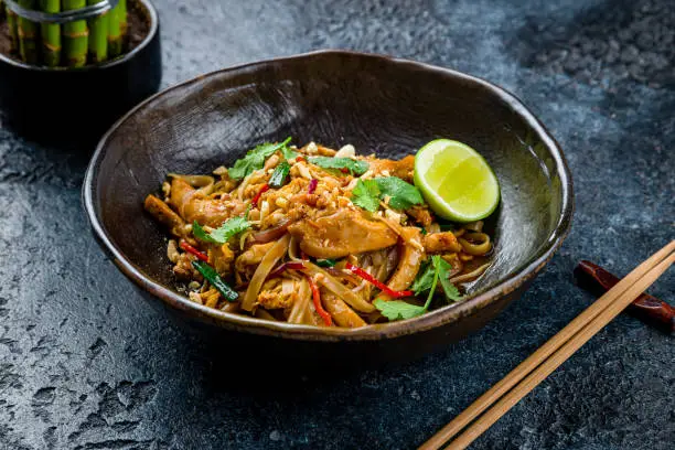 Photo of pad thai noodles with chicken on dark stone table