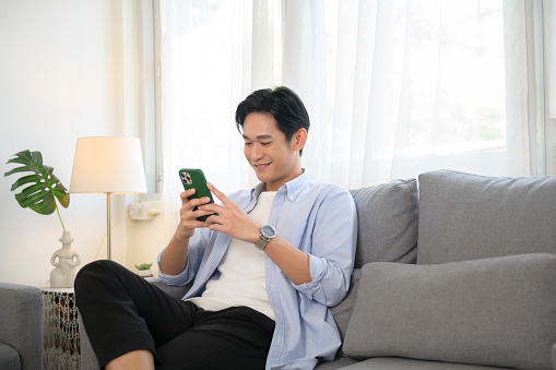 Young asian man using smart phone on sofa in living room