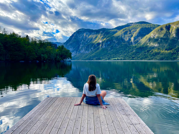 kobieta w średnim wieku cieszy się spokojną chwilą na molo nad brzegiem jeziora bohinj w słowenii - lake bohinj zdjęcia i obrazy z banku zdjęć