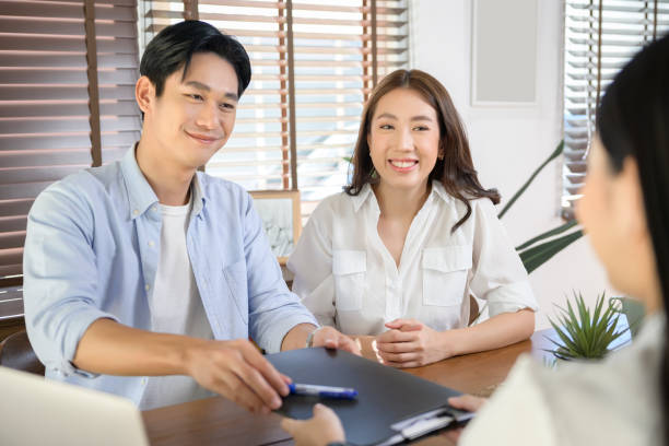 Young married couple meeting with female real estate agent or insurance consultant offering promotions , Mortgage, loan, property and medical health insurance concept. stock photo