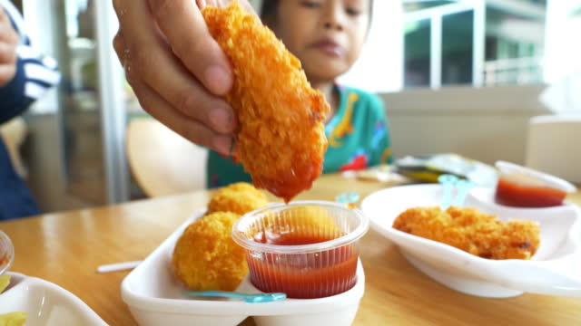 Asian boy dipping fried chicken in sauce .