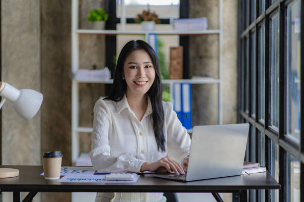 istock Asian businesswoman working on laptop computer with financial graph document in modern office near window with calculator and business report on desk 1432085604