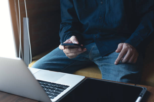 istock Young man sitting in coffee shop, using mobile phone browsing internet with laptop computer and digital tablet on table, male freelancer working at cafe 1432094244