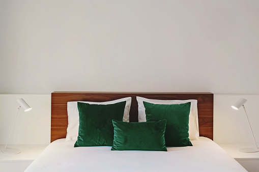 Modern bedroom in white colors with wooden headboard and green velvet accent pillows