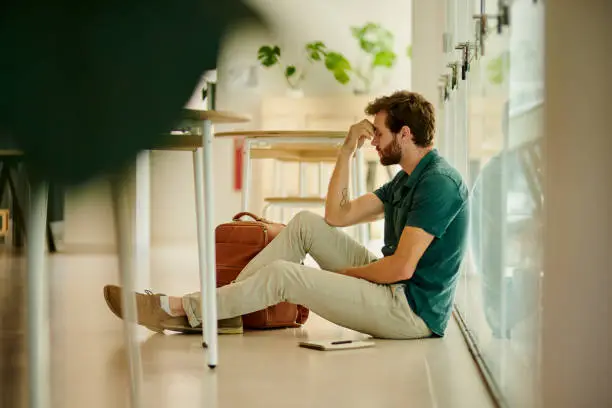 Photo of Anxiety, stress and student at university with anxiety for test. Young man with headache, worried and frustrated sitting on the floor. Burnout in education, learning and stressed with exam or result