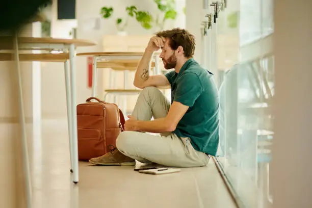 Photo of Anxiety, depression and stress student with burnout, sad and thinking about exam, university and debt at campus. Mental health, education and depressed man sitting on the floor at college or school