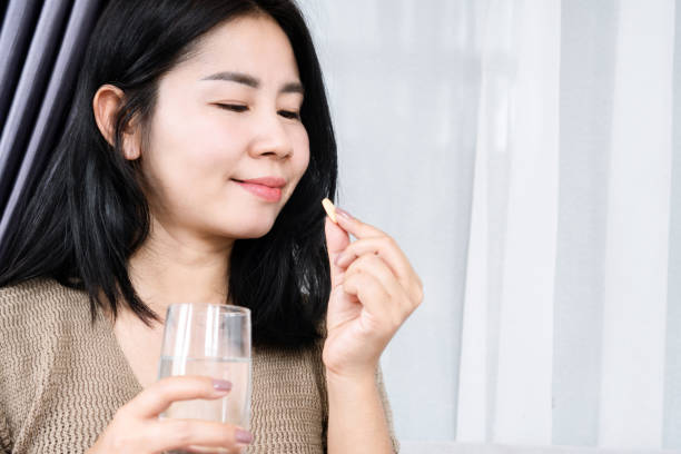 mujer asiática que toma vitamina c con un vaso de agua - vitamin pill vitamin c nutritional supplement bottle fotografías e imágenes de stock