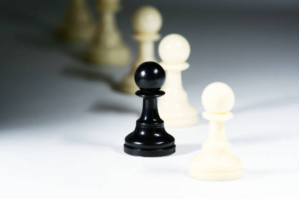 One black pawn chess piece standing alone alongside a line of many white pawns.