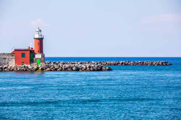 Lighthouse by the sea with rocks at the port of Ischia in Italy. Wide view.