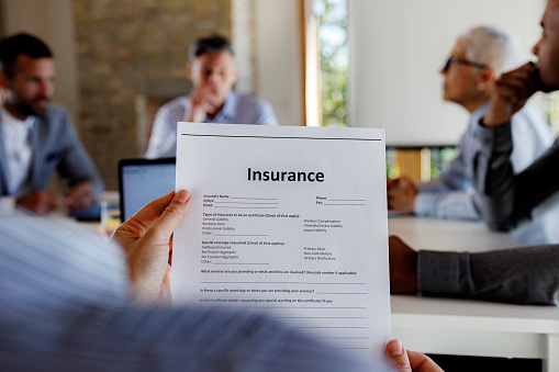 Close up of unrecognizable person reading documents of insurance in the office. There are people in the background.