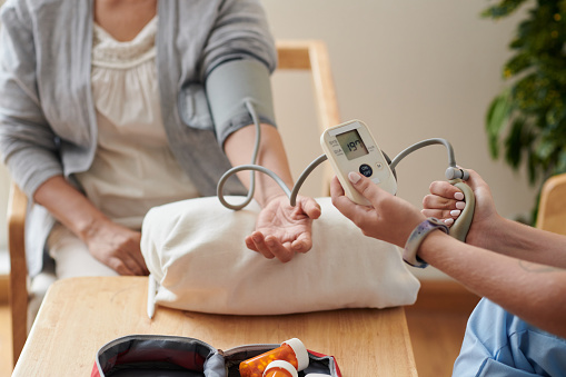 Close-up of nurse checking blood pressure of patient with special medical equipment at table