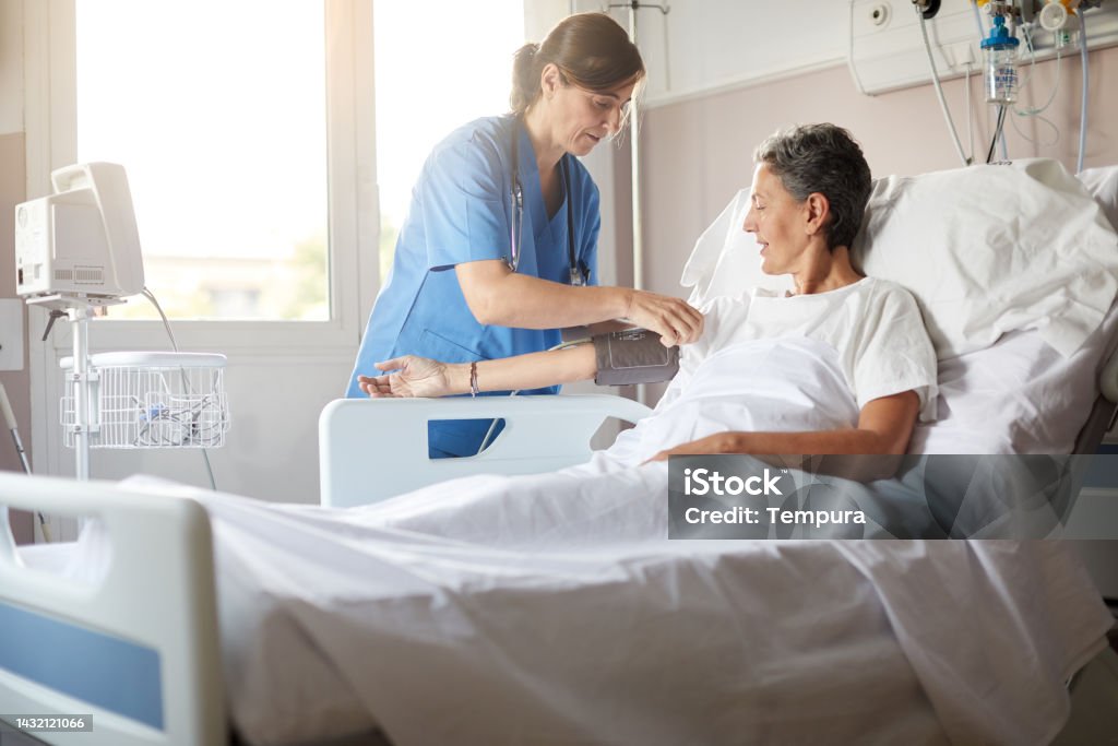 Female nurse adjusting the blood pressure monitor on female hospital patient Photo with copy space of female nurse leaning over bedside while attaching the blood pressure armband to a female patient's right arm. Nurse Stock Photo